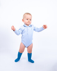 Beautiful blond baby boy wearing blue standing against white background smiling and looking to the camera. 