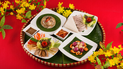 Family dinning table of Tet holiday or Lunar New Year with traditional foods: pork belly and eggs braised in coconut water, pickles, rice, Banh Tet (rice cake), fried vegetables, bitter melon soup. 