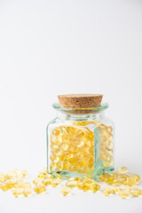 View on white background glass bottle with yellow evening primrose oil pills, vertical, with copy space