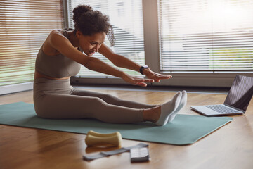 Woman doing stretching exercise online using laptop at home. Indoors workout, yoga, pilates project