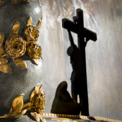 Ein Kruzifix mit einer hockenden Person davor als Schattenwurf. Im Vordergrund sind goldene Blumen...