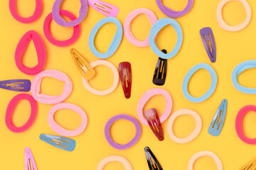 Many small multicolored hair scrunchies and clips on a yellow background.