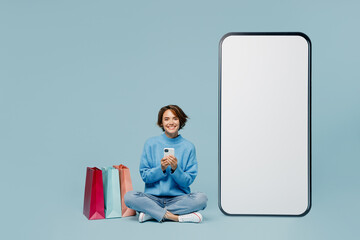 Full body young woman in knitted sweater near package bags after shopping big huge blank screen...