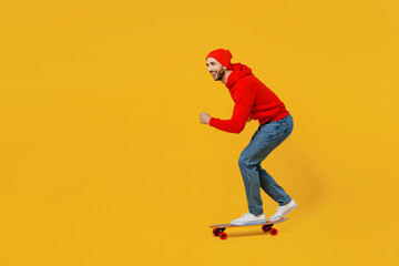 Full body side profile view smiling happy young caucasian man wear red hoody hat riding skateboard...