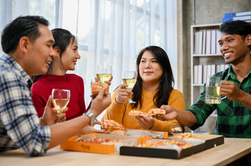 Group of happy and joyful Asian coworkers drinking wine and eating pizza in the office.