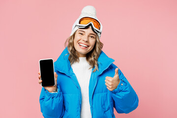 Snowboarder woman wear blue suit goggles mask hat ski jacket hold mobile cell phone blank screen show thumb up isolated on plain pastel pink background. Winter extreme sport hobby trip relax concept. © ViDi Studio