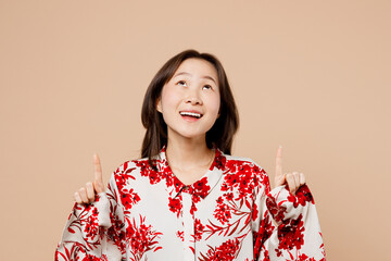 Young woman of Asian ethnicity wear red shirt point index finger overhead indicate on workspace...