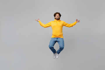 Fototapeta na wymiar Full body young Indian man 20s he wearing casual yellow hoody jump high hold spreading hands in yoga om aum gesture relax meditate try to calm down isolated on plain grey background studio portrait