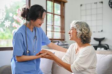 Obraz premium Caring and kind young Asian female doctor or nurse holding an aged female's hands to comfort