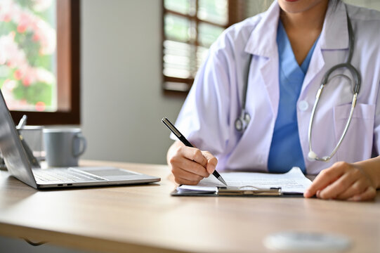 cropped image. Smart Asian female doctor taking notes or filling medical form at her desk.