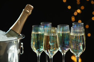 Glasses of champagne and ice bucket with bottle on black background