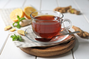Cup of delicious ginger tea and ingredients on white wooden table, closeup