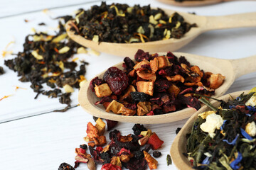 Spoons with dried herbal tea leaves and fruits on white wooden table, closeup