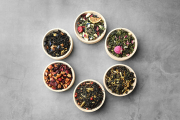 Different kinds of dry herbal tea in wooden bowls on light grey table, flat lay. Space for text