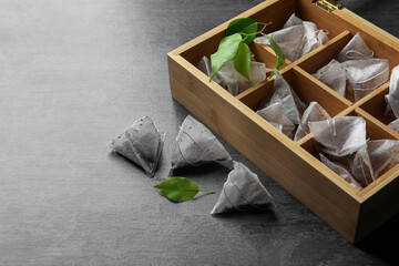 Wooden box with paper tea bags and leaves on dark grey table, space for text