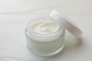 Glass jar of face cream on white marble table