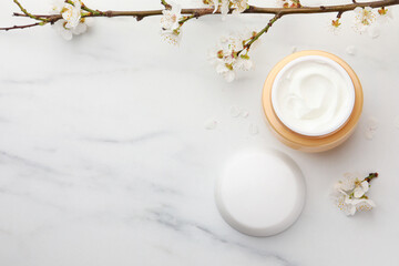 Jar of face cream, tree branch and flowers on white marble table, flat lay. Space for text