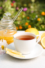 Cup of delicious tea with honey, lemon and chamomile on white table outdoors