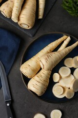 Whole and cut parsnips on black table, flat lay