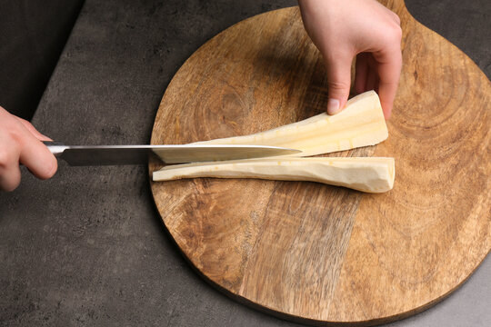 Woman cutting delicious fresh ripe parsnip at black table, closeup