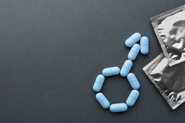 Male sign made of pills and condoms on dark gray background, flat lay with space for text. Potency...