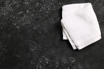 Soft folded terry towel on black textured background, top view. Space for text