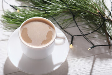 cup of coffee with milk on a wooden table with pine tree branch and light garland decor. cozy christmas morning concept.