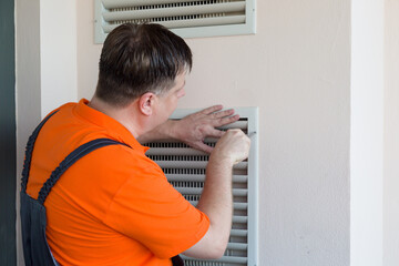 A serious master screws grate from ventilation system to the wall.