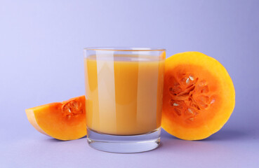 Tasty pumpkin juice in glass and cut pumpkin on lavender color background