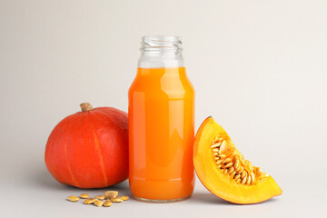 Tasty pumpkin juice in glass bottle, whole and cut pumpkins on light background