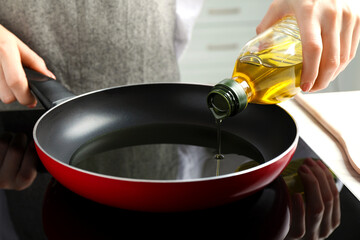 Woman pouring cooking oil from bottle into frying pan on stove, closeup