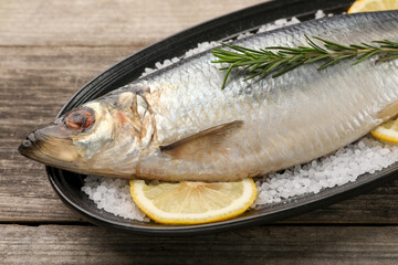 Plate with salted herring, rosemary and lemon on wooden table, closeup
