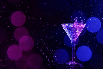 Glass of martini and splashes in neon lights on dark background, bokeh effect with space for text