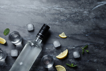 Fototapeta na wymiar Bottle of vodka, shot glasses, lemon, mint and ice on black marble table, flat lay. Space for text