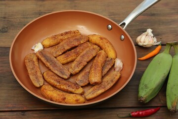 Delicious fried bananas, fresh fruits and different peppers on wooden table