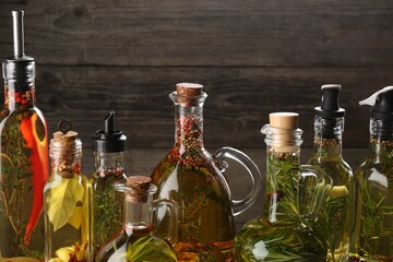 Cooking oil with different spices and herbs in bottles on wooden background