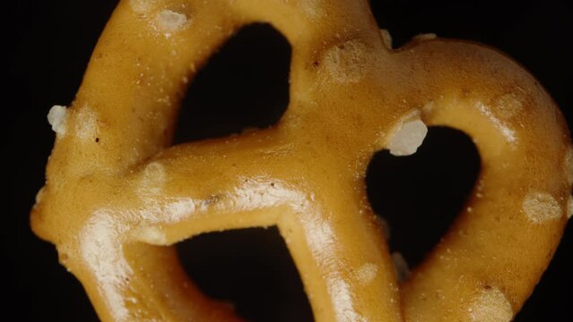 Salty mini pretzel, spinning on a black background, looks like it's falling down, super close-up. Slow motion