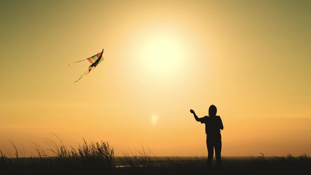 teenage girl flies kite into sky sunset. happy childhood. childhood dream fly. kite flies wind glare sun. concept happy childhood dream girl. outdoor play children toy. carefree freedom nature.