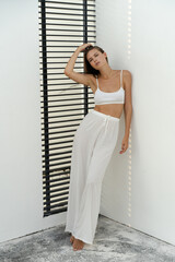Fashion  photo of stylish brunette woman in white  homewear. Linen pants and crop top. Posing on...
