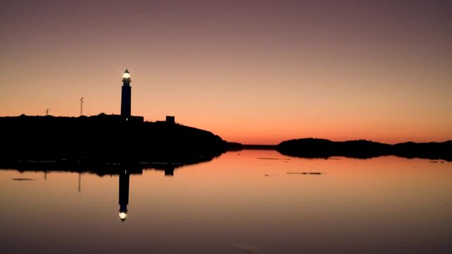 Shot Of Lighted Lighthouse At Clear Sky Night in Cadiz with the lighthouse reflected in the water