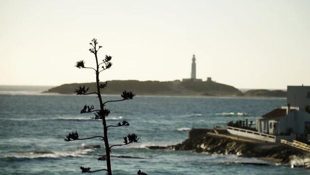 Distance out of focus Trafalgar light house standing on the big island as the waves move in slow motion 