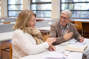 Portrait of joyful elderly people discussing lecture. Caucasian man and woman sitting in library after classes reading books analyzing material doing tasks. Education and studying for adults concept