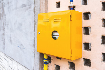 Gas meter in yellow metallic box attached to a wall of house