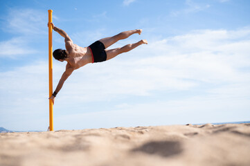 Young man doing the flag exercise on the beach. Calisthenics concept.