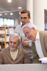 Portrait of happy aged men studying with instructor. Two grey-haired man beginning day with classes and tasks, teacher teaching them how to use computer. Modern technologies and adult people concept