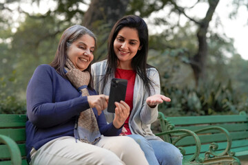 Two indian woman in warm wear and talking on video call at park.