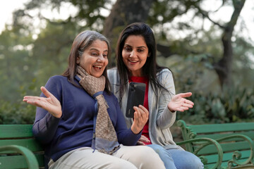 Two indian woman in warm wear and talking on video call at park.