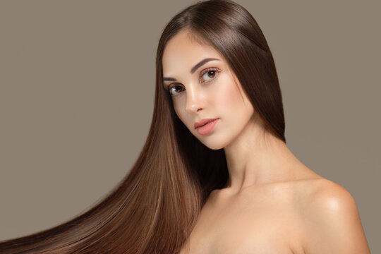Portrait of a beautiful young brunette woman with long straight hair. On a gray background