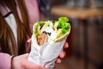greek meat gyros with tzatziki sauce, vegetables, feta cheese and french fries in woman hand. street food