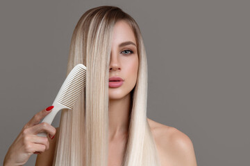 beautiful young woman holds a comb in her hands. Blonde woman with long straight hair on a gray...